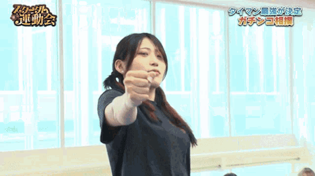 a woman in a blue shirt is pointing her finger at someone in a room with chinese writing on the wall behind her