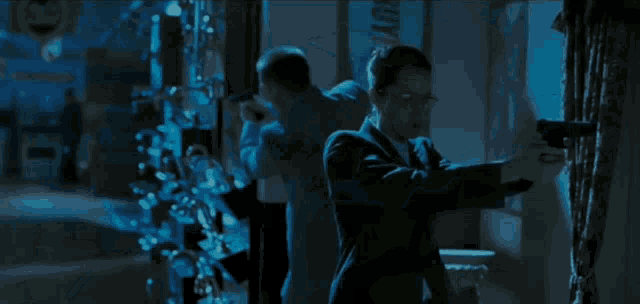 a woman in a suit is kneeling down next to a man laying on the floor in a dark room
