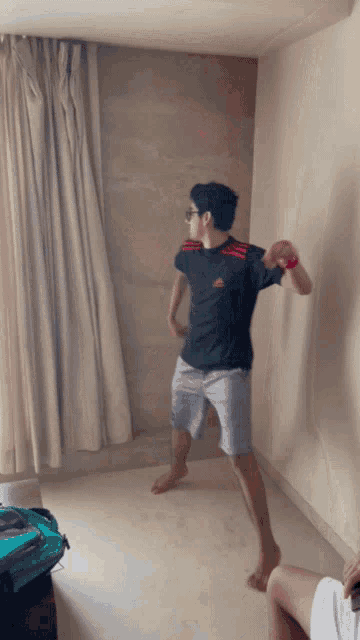 a young man in a black adidas shirt is dancing in a room