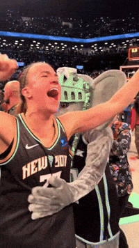 a woman wearing a new york jersey celebrates with a mascot
