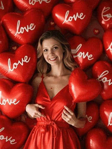 a woman in a red dress holds a heart shaped balloon in front of a wall of love balloons