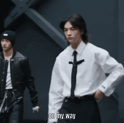 a man in a white shirt and black tie says " on my way " while standing next to another man