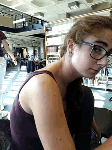 a woman wearing glasses and a purple tank top is sitting in a library