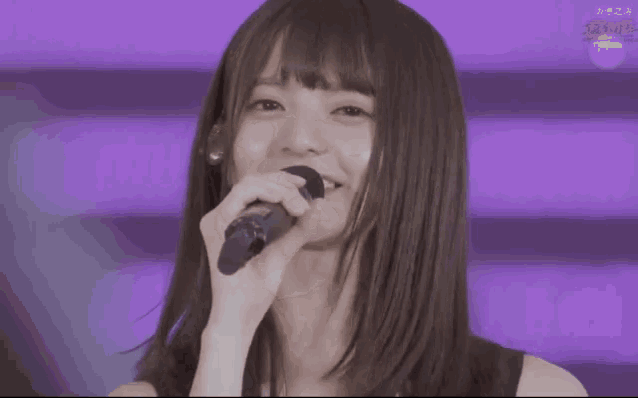 a young woman singing into a microphone with chinese writing on the screen behind her