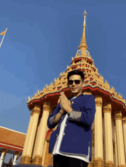 a man wearing sunglasses and a blue jacket is standing in front of a temple