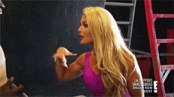 a blonde woman in a pink top is pointing at something .