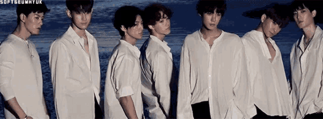 a group of young men in white shirts are standing next to each other on the beach .