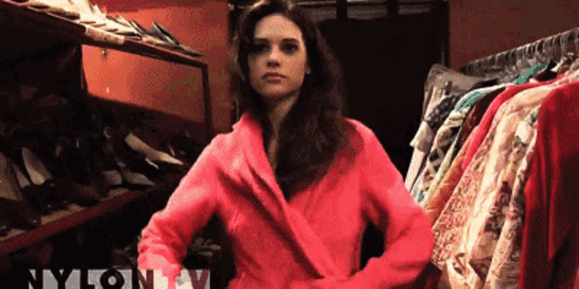a woman in a pink coat is standing in front of a rack of clothes with the word nylon on the bottom