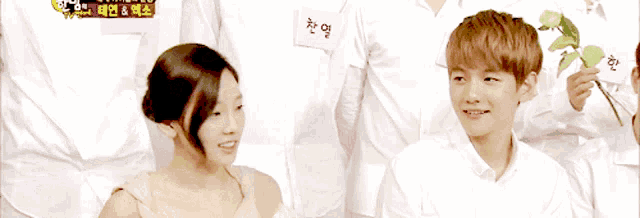 a man and a woman are sitting next to each other and the woman is wearing a flower arrangement