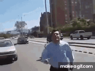 a man in a blue shirt is running down a street with cars behind him