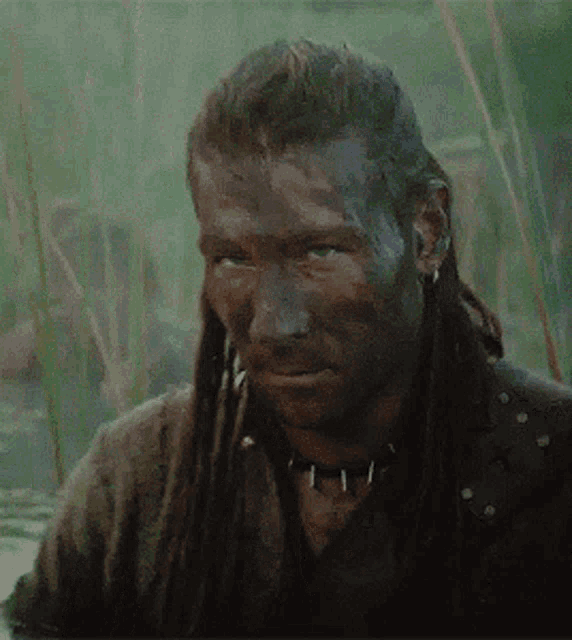 a man with dreadlocks is covered in mud and has a choker around his neck