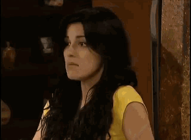 a woman with long black hair is wearing a yellow shirt and talking to someone while sitting at a table .
