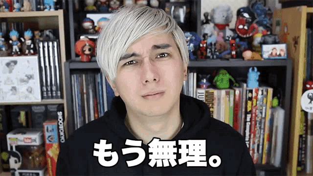 a man in a black hoodie stands in front of a shelf full of books including one that says tokyo