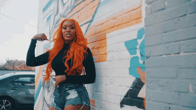 a woman with orange hair is standing in front of a wall with graffiti on it