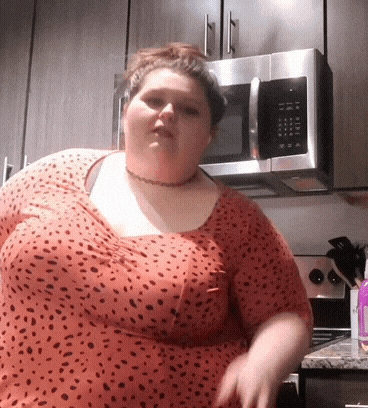 a woman is standing in a kitchen with a microwave in the background .