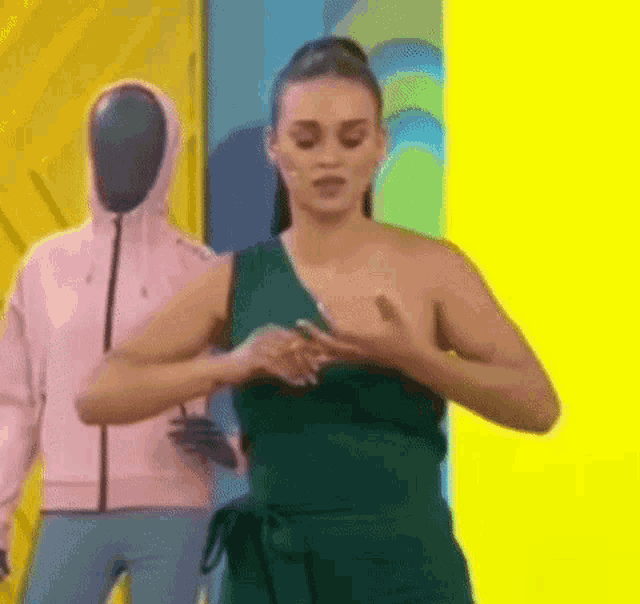 a woman in a green dress is standing in front of a yellow wall with a mannequin in a pink jacket .