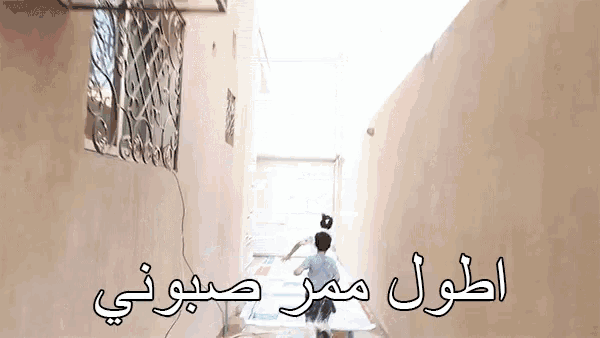 a boy is running down a hallway with arabic writing on the wall behind him