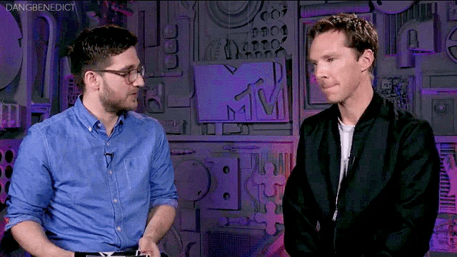 two men are talking in front of a wall with a mtv logo