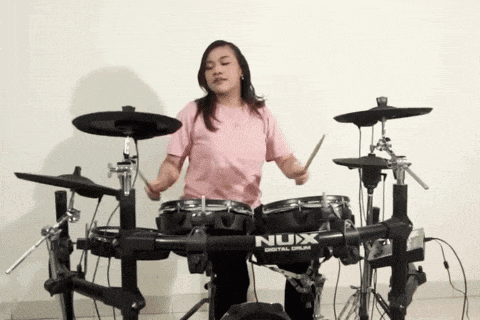 a woman in a pink shirt is playing a nux drum set