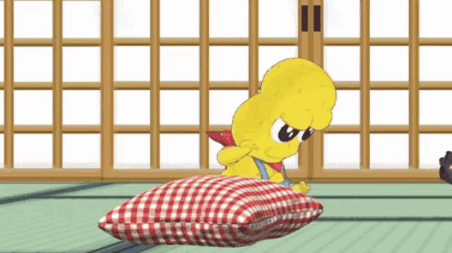 a yellow cartoon character sitting on a red and white checkered pillow
