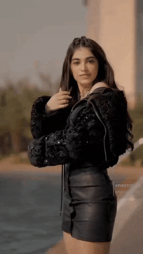 a woman in a black jacket and black leather skirt is standing next to a body of water .