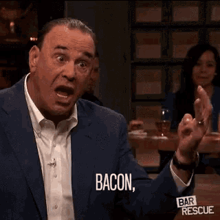 a man in a suit and white shirt is sitting at a bar talking about bacon .