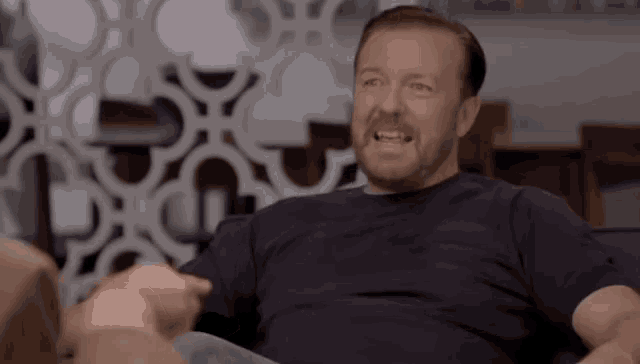 a man with a beard is sitting on a couch and making a funny face