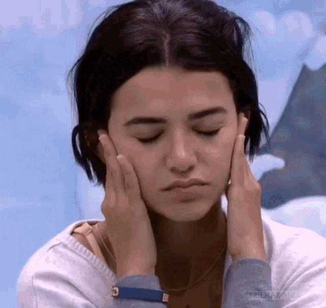 a woman is holding her face with her hands while looking down .