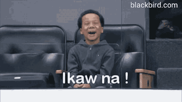 a young boy is sitting in a stadium and laughing with the words " ikaw na " written above him