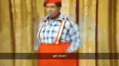 a man wearing a red hat and suspenders is standing in front of a curtain and says get down .