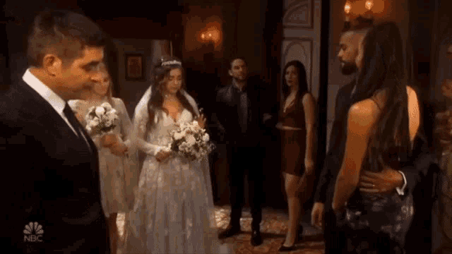 a bride and groom are standing next to each other in a room while their wedding party looks on .