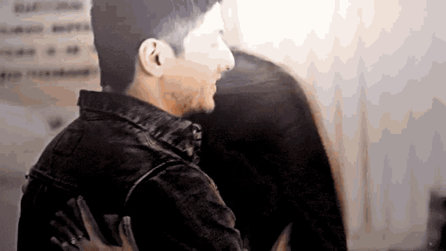 a man in a leather jacket is hugging another man in a room .