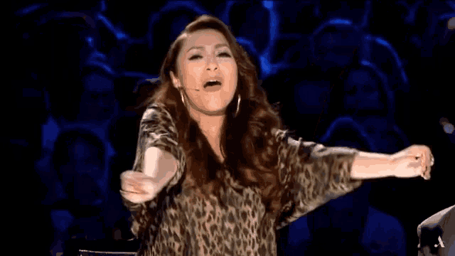 a woman in a leopard print shirt holds her arms up in the air