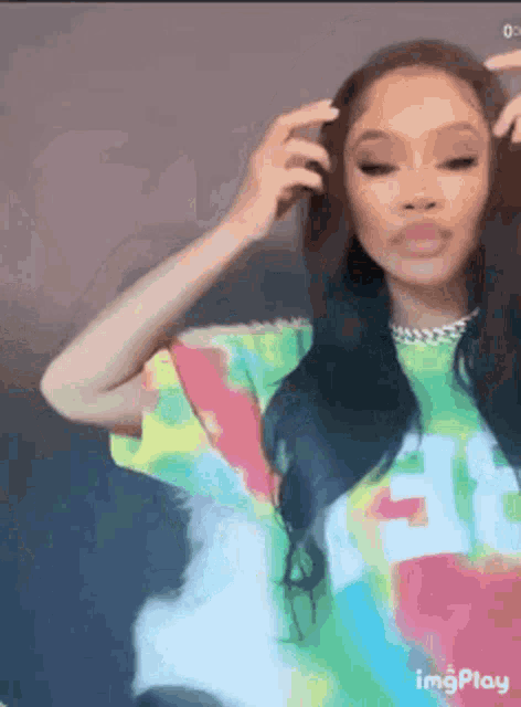 a woman in a colorful tie dye shirt is holding her hair .