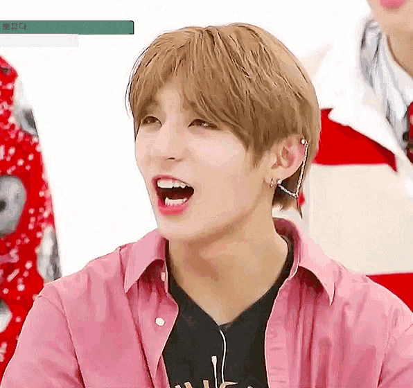a young man wearing a pink shirt and ear piercings is laughing