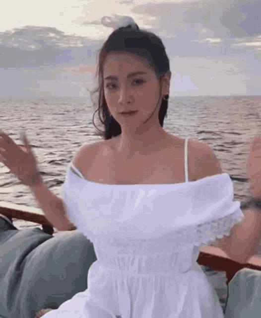 a woman in a white dress sits on a boat in the ocean