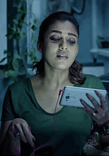 a woman in a green shirt is holding a cell phone in her hand .