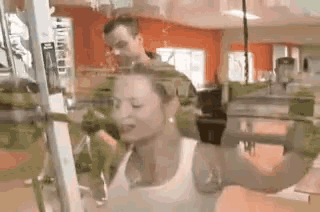 a woman is lifting a dumbbell in a gym while a man watches