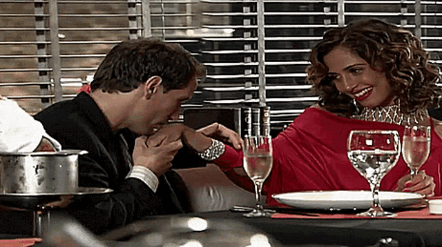 a man kisses a woman 's hand at a table with wine glasses
