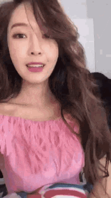 a woman with long hair is wearing a pink off the shoulder top and smiling .