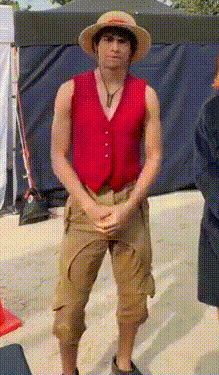 a man wearing a hat and a red vest is standing on a sidewalk .