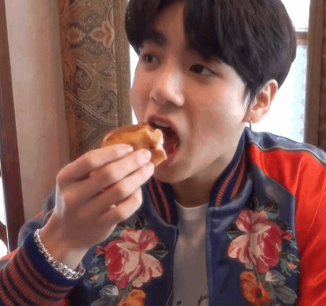 a young man wearing a floral jacket is eating a piece of bread