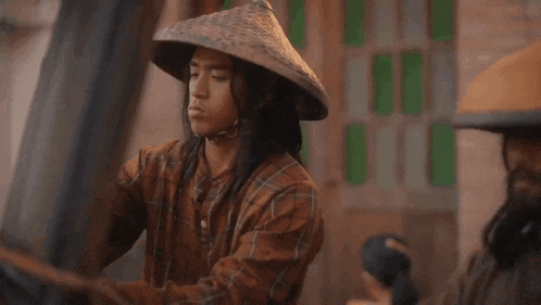 a man with long hair wearing a conical hat is standing next to another man .