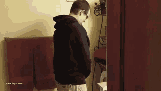 a man in a black hoodie is standing in a bathroom looking at his pants .