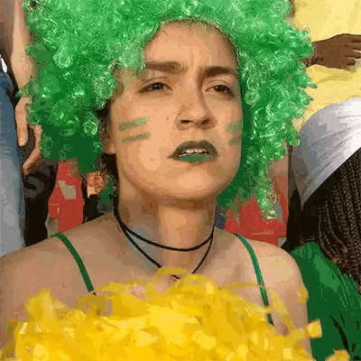 a woman wearing a green wig and green paint on her face is holding a bunch of yellow pom poms