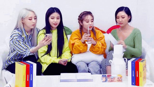 four girls are sitting on a couch looking at their phones .