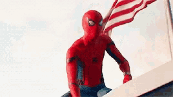 a man in a spiderman costume is holding an american flag while standing on top of a building .