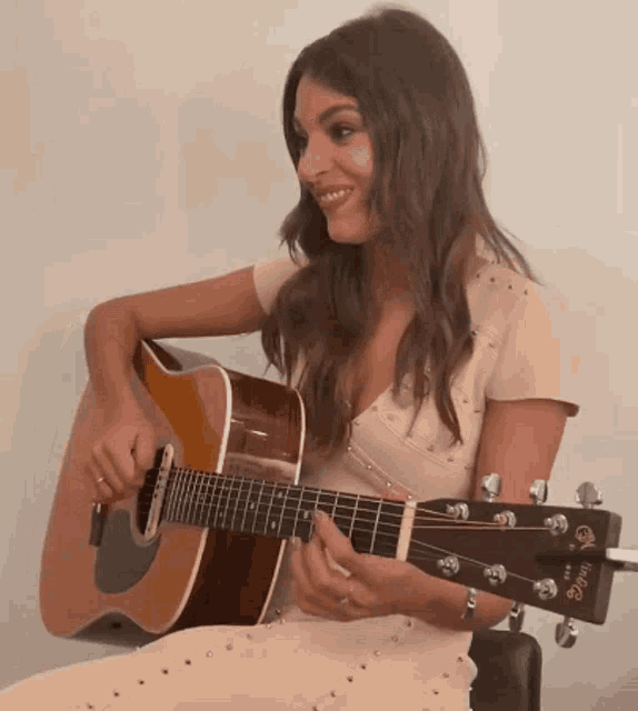 a woman in a white dress is playing an acoustic guitar with a taylor logo on the headstock