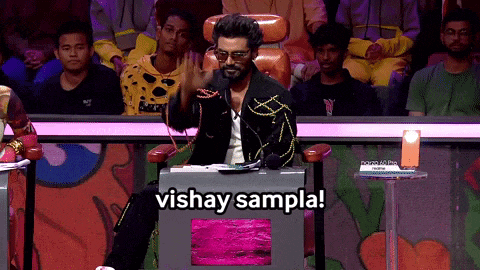 a man sitting in front of a crowd with the words vishay sampla written below him