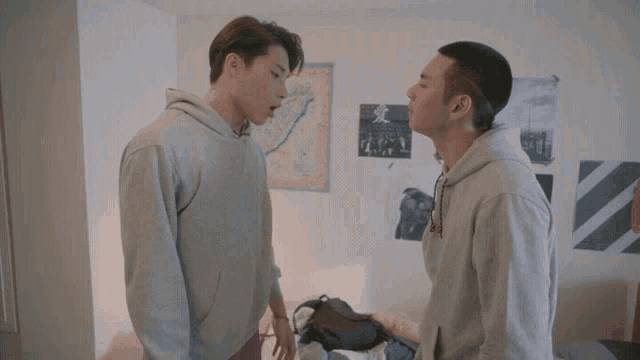 two men are standing next to each other in a bedroom with posters on the wall